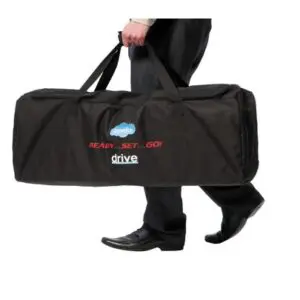 A person in black dress trousers and shoes carries a large black Drive TraveLite Aluminium Transport Chair case labelled "drive" and "READY...SET...GO!".