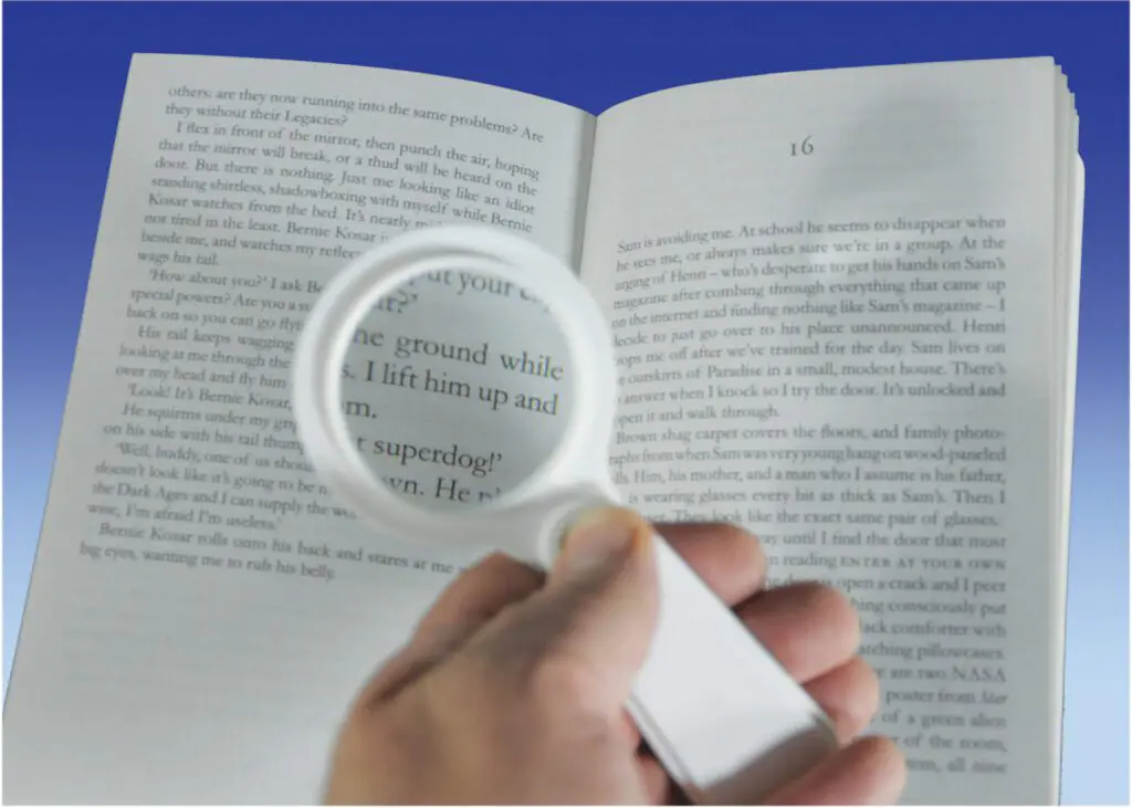 A person uses the Handheld Magnifier with Light to enlarge and illuminate the text in an open book.