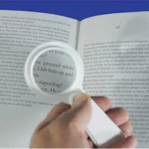 A person uses the Handheld Magnifier with Light to enlarge and illuminate the text in an open book.