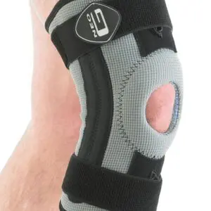 A person wearing the NEO G RX KNEE SUPPORT, a grey and black knee brace featuring an open patella design and adjustable straps.