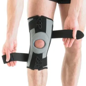 Individual adjusting the straps of the NEO G RX KNEE SUPPORT, a black and grey knee brace, around their knee.