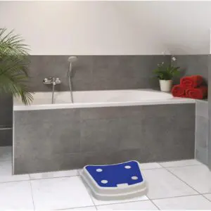 A grey-tiled bathroom with a bathtub, handheld showerhead, green plant, red towels, and a Plastic Stack-able Bath Step in blue and white on the floor.