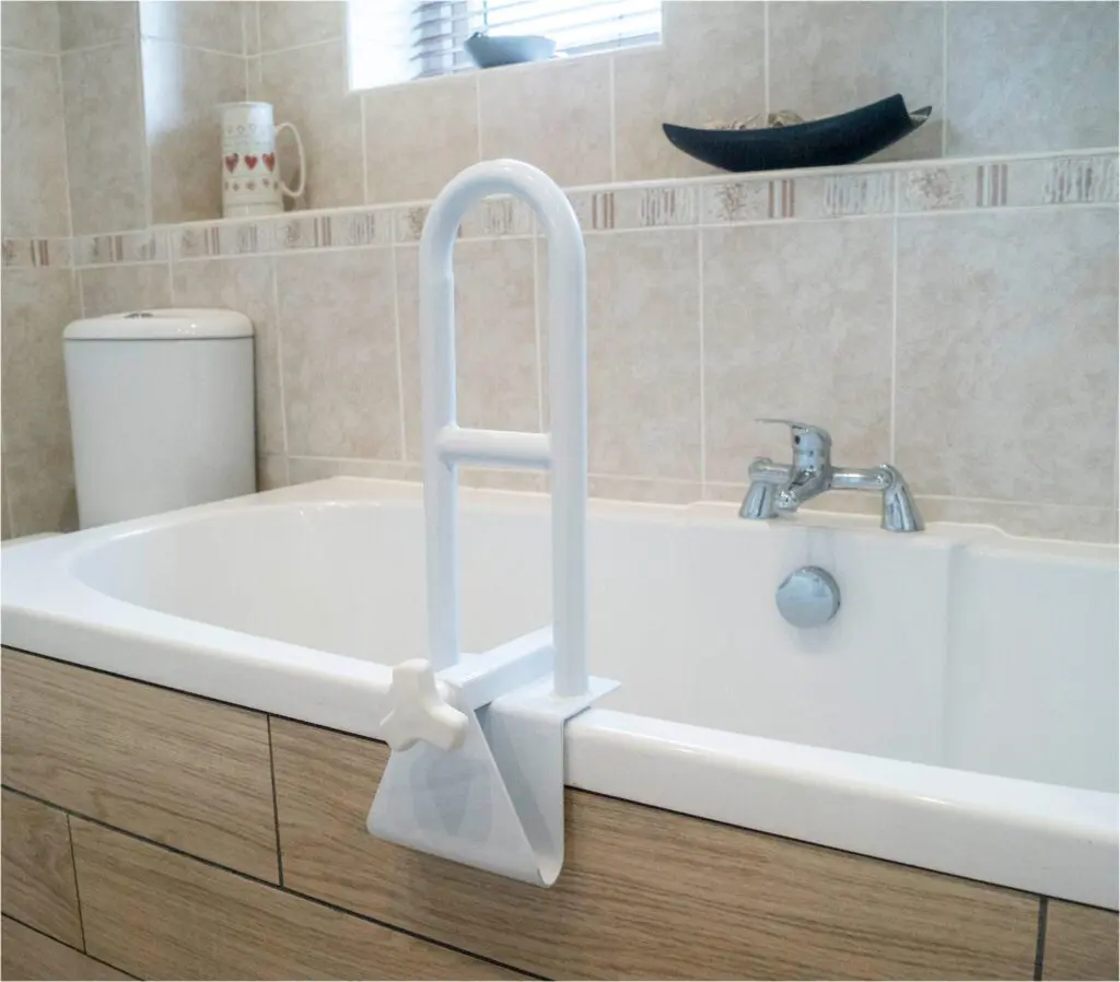 A Bath Grab Rail is installed on the edge of a bath in a tiled bathroom, with a toilet and tap seen in the background.