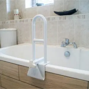 A Bath Grab Rail is installed on the edge of a bath in a tiled bathroom, with a toilet and tap seen in the background.
