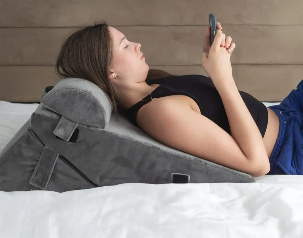A woman reclines on a bed, using the Luxury Folding Adjustable Bed Wedge Pillow for support whilst looking at her phone.