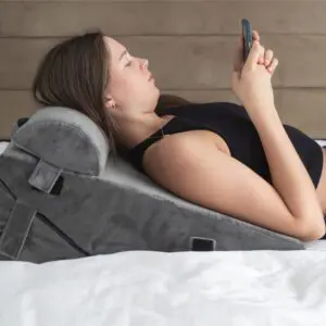 A woman reclines on a bed, using the Luxury Folding Adjustable Bed Wedge Pillow for support whilst looking at her phone.