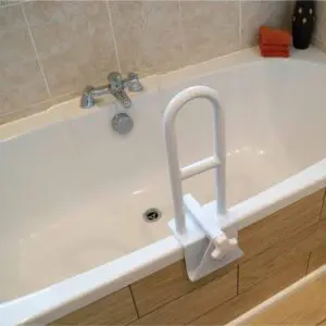 A white bath features a Bath Grab Rail mounted on the edge, a tap on the tiled wall, and two orange towels stacked in the corner.