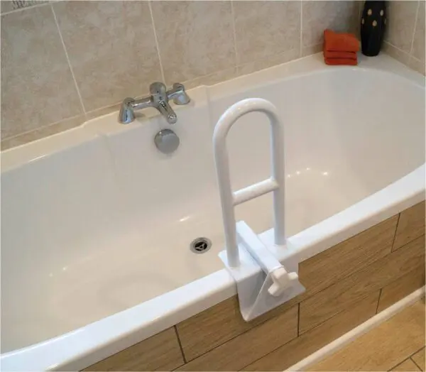 A white bath features a Bath Grab Rail mounted on the edge, a tap on the tiled wall, and two orange towels stacked in the corner.