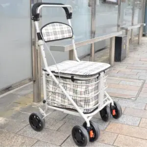 A checked-patterned wheeled shopping trolley with a seat is parked on a pavement near a glass bus shelter.
