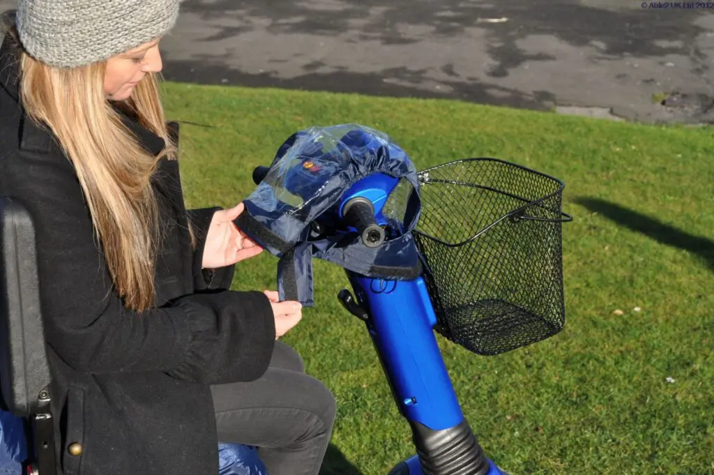 A woman on a mobility scooter attaches the blue Splash Scooter Control Panel Cover to the scooter's control panel and handlebars.