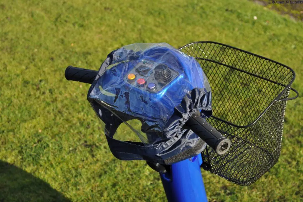 Electric scooter handlebars with a transparent plastic cover over the control panel and a metal basket attached at the front, positioned on grass.
