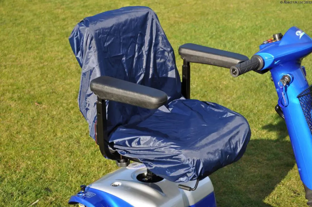 A blue mobility scooter with a blue protective cover on the seat, parked on green grass in daylight.