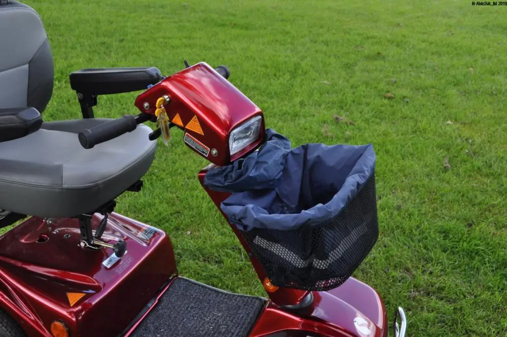 Red mobility scooter with a grey seat, black armrests, and a front basket, parked on grass.
