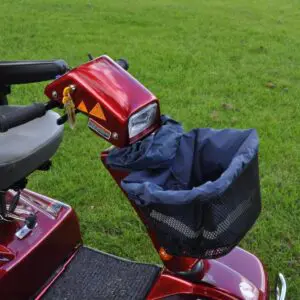Red mobility scooter with a grey seat, black armrests, and a front basket, parked on grass.