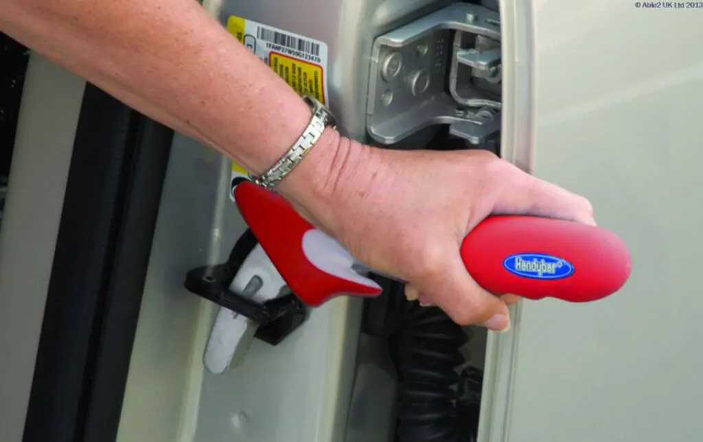 A person uses the Handybar, a red device inserted into the car door catch, to assist with getting in or out of a vehicle.