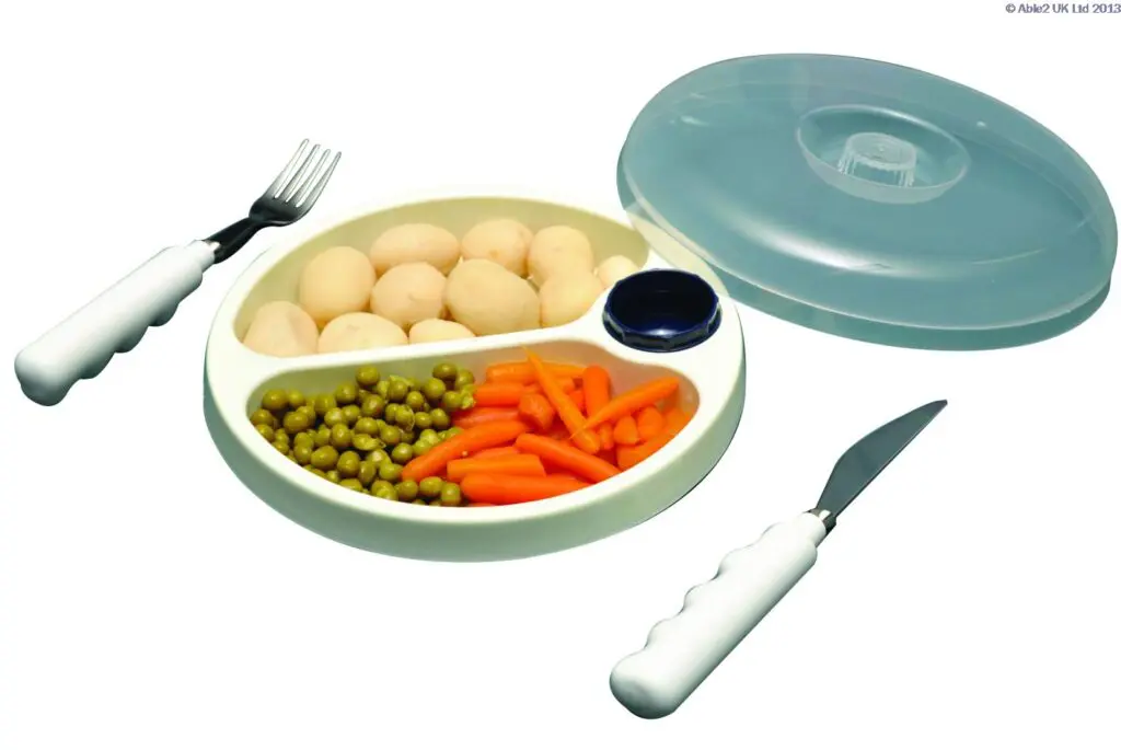 The Stay Warm Feeding Dish includes a divided plate with potatoes, peas, and carrots, a small bowl of sauce, large-handled fork and knife, and a clear plastic lid.