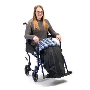 Woman sitting in a wheelchair with a Padded Leg Cosy over her legs and a checked blanket on her lap, facing forward and smiling.