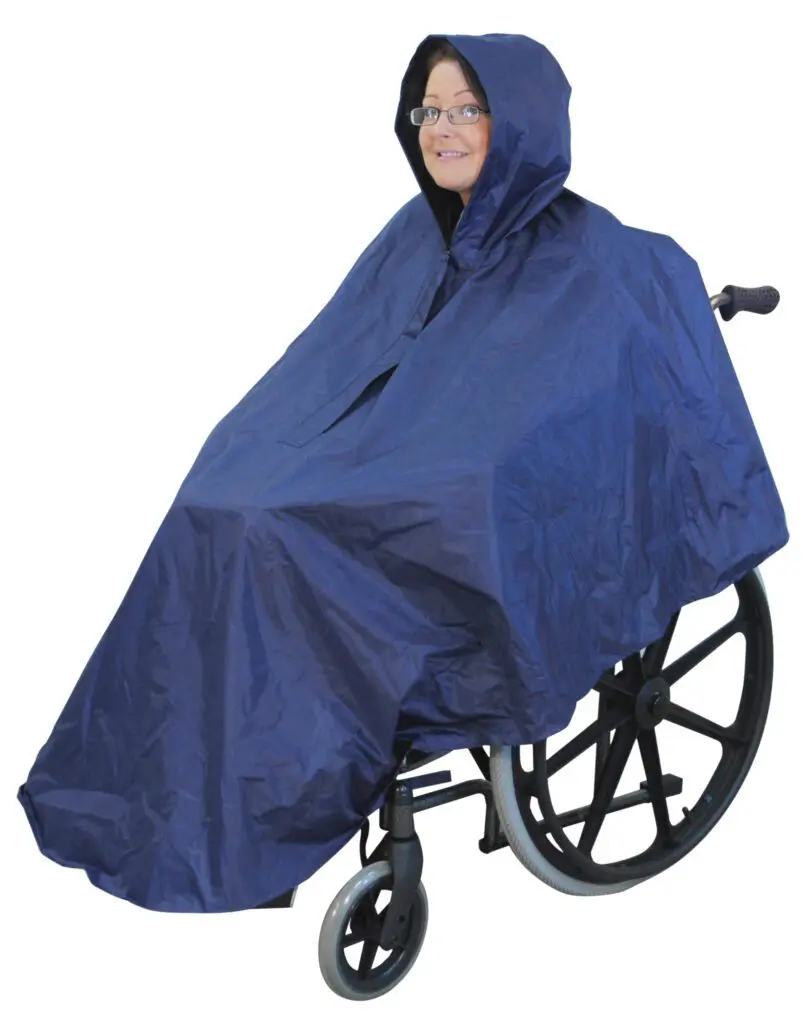 A person in a wheelchair wears the Wheelchair Poncho, a navy blue hooded rain poncho designed to cover both user and wheelchair.
