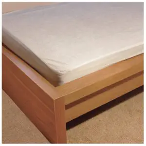 A close-up of a wooden bed frame featuring the Anti-Allergenic Waterproof Mattress Protector King-size on a white mattress, set on a beige carpeted floor.