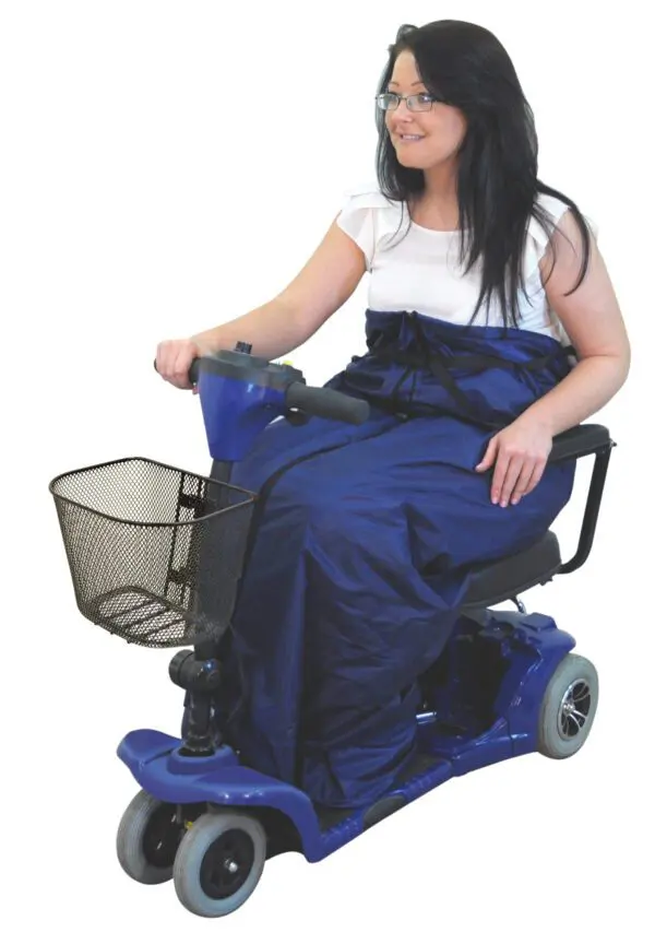 A woman sits on a blue mobility scooter, staying warm with the Fleece Lined Scooter Cosy while holding the handlebars. The scooter features a front basket.