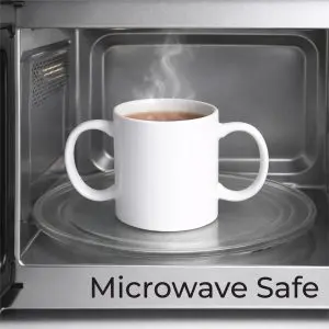A white mug with two handles sits on a glass turntable inside a microwave, with steam rising. The words "Microwave Safe" are written at the bottom.