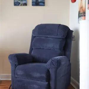 A blue upholstered reclining chair sits in the corner of a room with light walls, wooden flooring, and framed artwork on the wall above.