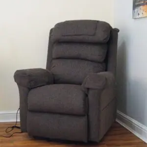 A dark grey recliner chair is positioned in the corner of a room with wooden flooring. Two paintings and a red wall clock are hung on the walls above and beside the chair.