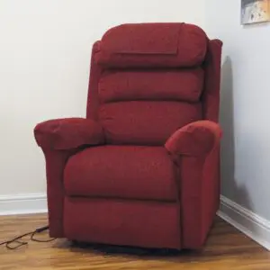 A red upholstered reclining chair sits on a wooden floor in the corner of a room, with paintings and power leads visible nearby.
