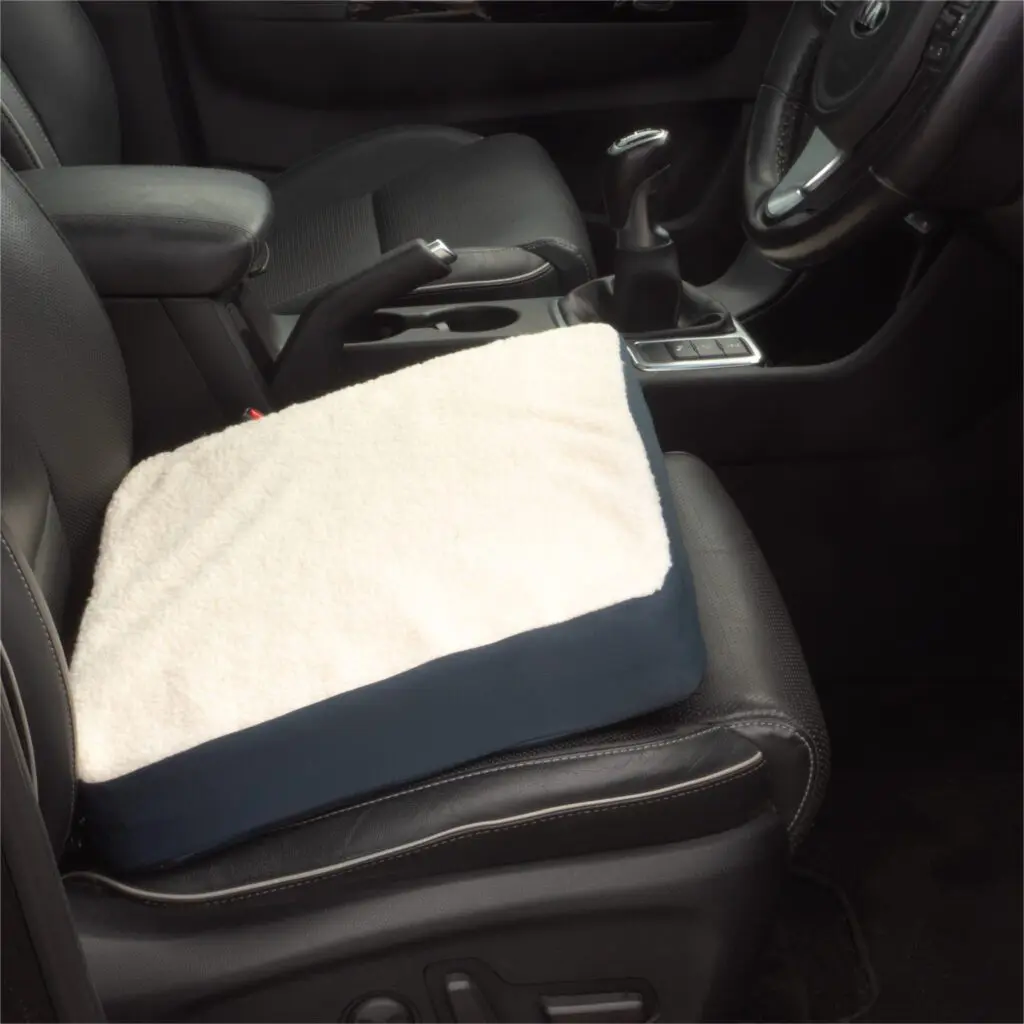 A Gel Comfort Cushion with a white cover is placed on the driver’s seat of a black car interior.