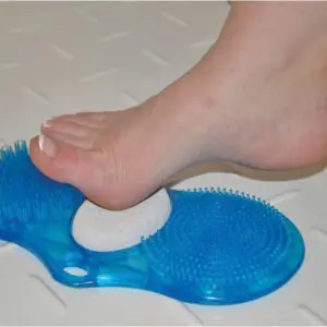 A bare foot rubs against the Foot Cleaner with pumice, a blue plastic scrubber with bristles and a pumice stone, on a white textured surface.