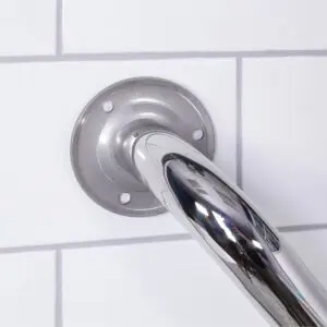 Close-up of the stainless steel grab rail in a polished finish, securely mounted on a white tiled wall with visible bolts at the base plate.