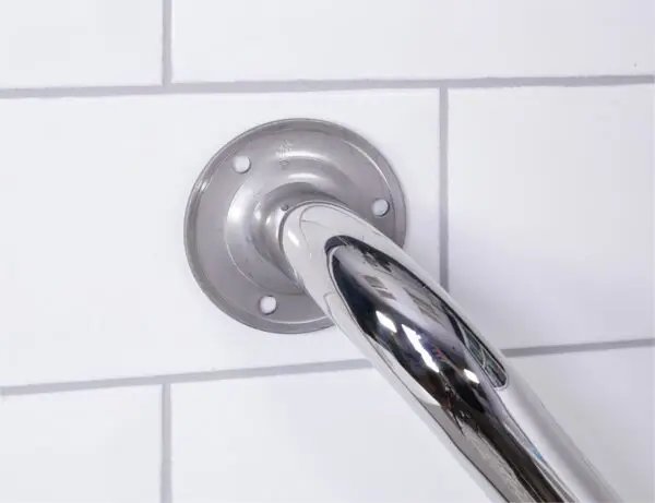 Close-up of the stainless steel grab rail in a polished finish, securely mounted on a white tiled wall with visible bolts at the base plate.
