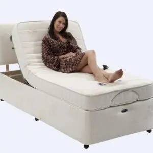 A woman in a spotty dressing gown sits on an adjustable bed with the head section raised, smiling at the camera.