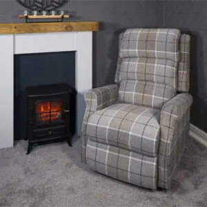 The Broadway Dual Motor Rise and Recline Chair sits next to an electric fireplace in a carpeted room with grey patterned walls and a wooden mantelpiece.