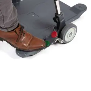 A person wearing brown dress shoes presses a pedal on the base of the Motion Transfer Aid near its rear wheel.