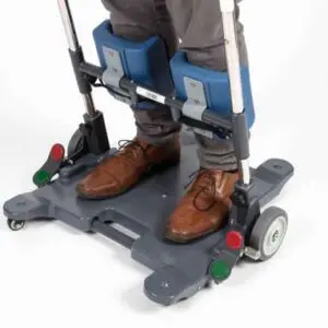 A person stands on the Motion Transfer Aid, a device with padded knee supports and wheels designed for safe patient transfers.