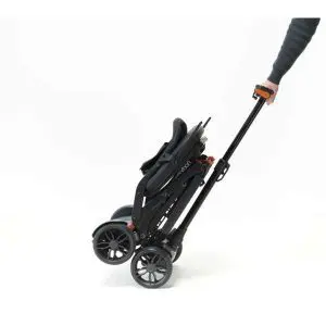 A person pulls a folded black pushchair by its handle on two wheels against a white background.