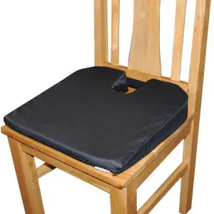 A wooden chair with a Coccyx Wedge Cushion featuring a black seat and U-shaped cut-out at the back.