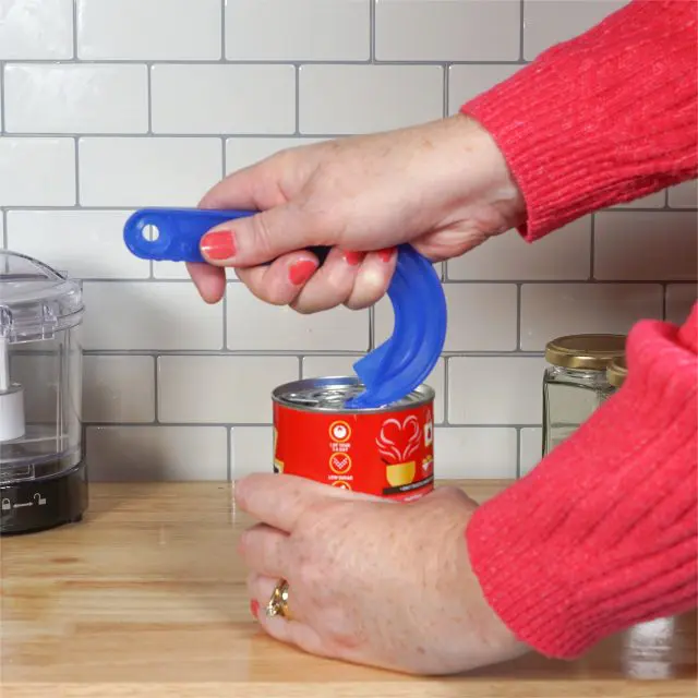 A person uses a Ring Pull Tin Opener to open a tinned food item on a wooden kitchen worktop in front of a white tiled splashback.