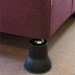 A close-up of a sofa leg placed inside a black plastic raiser on a carpeted floor.
