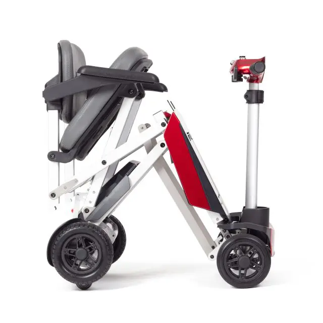 The Manual Fold+ wheelchair is shown in a folded, compact position with visible wheels, seat, and frame, featuring red and black accents against a white background.