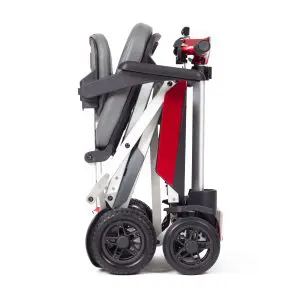 The Manual Fold+ is a compact, foldable mobility scooter featuring a grey seat and red frame, displayed here fully folded for convenient transport or storage.