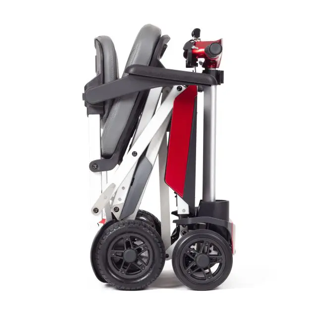 The Manual Fold+ is a compact, foldable mobility scooter featuring a grey seat and red frame, displayed here fully folded for convenient transport or storage.