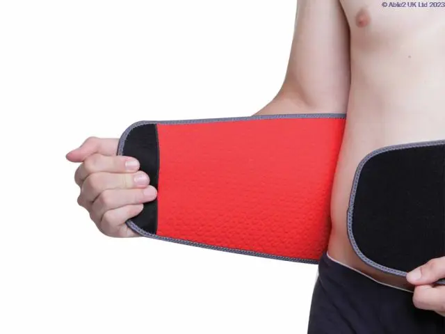 A person wearing the Aero-Tech Neoprene Advanced Back Support - Universal, fastening it around their waist with one hand, against a white background.
