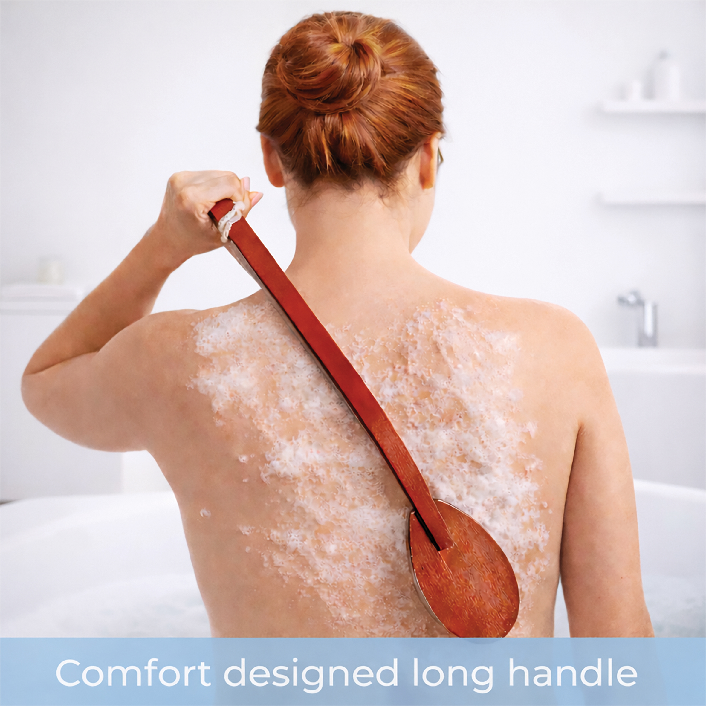 A person with red hair uses the Long-Handled Wooden Bath Brush to scrub their back whilst sitting in a bath filled with lathered soap.