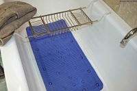 A white bath with a blue non-slip mat, a metal bath rack holding a brown towel, and a silver tap on the right side.