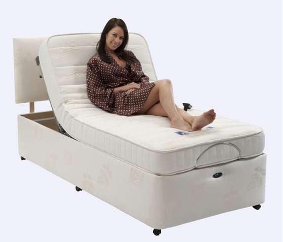 A woman in a brown polka dot dressing gown sits on the Richmond Electric Adjustable Bed with both the back and legs elevated.