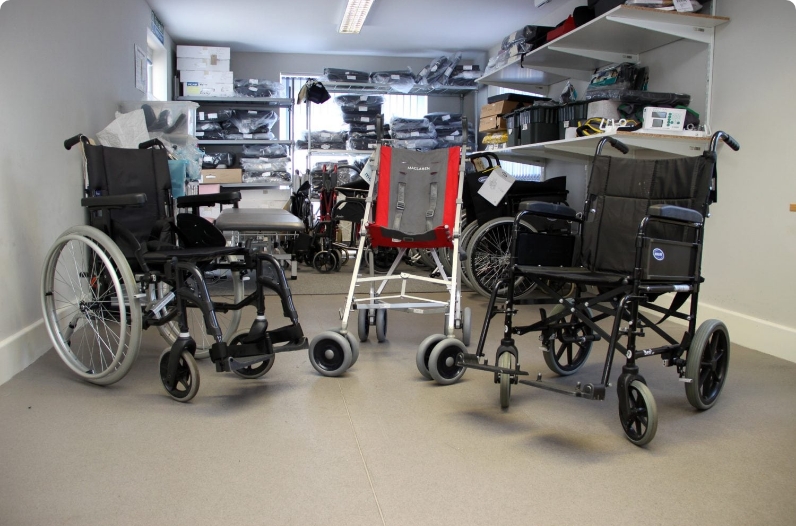 Three empty wheelchairs are arranged in a medical supply room with shelves filled with equipment and supplies in the background.