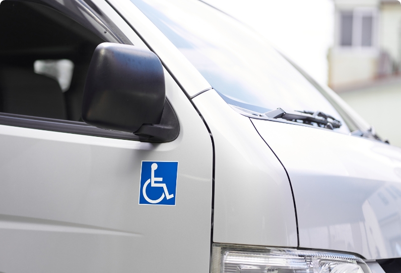 A close-up view of a white vehicle displaying a blue wheelchair accessibility symbol on its side near the front door.