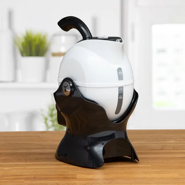 A Uccello Kettle, featuring a white and black egg-shaped design with a handle, sits on a wooden surface in a modern kitchen.